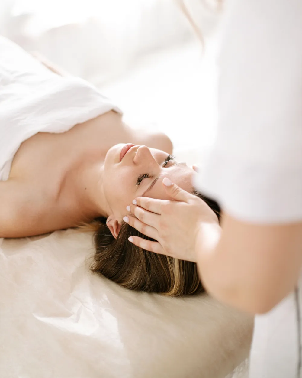 Guest lying on a massage table with her eyes closed while a therapist works gently along her brow and temple at Yoshino Massage in Arlington, TX